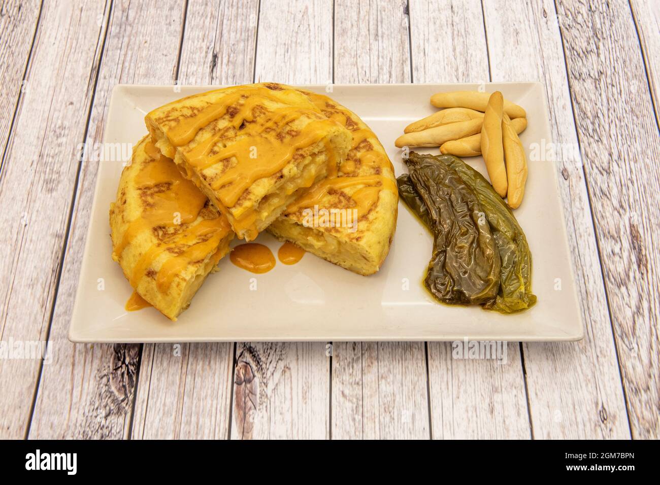 Beliebtes spanisches Kartoffelomelett, begleitet von geröstetem Paprika, Peaks und Käsesoße auf einem weißen Tablett Stockfoto