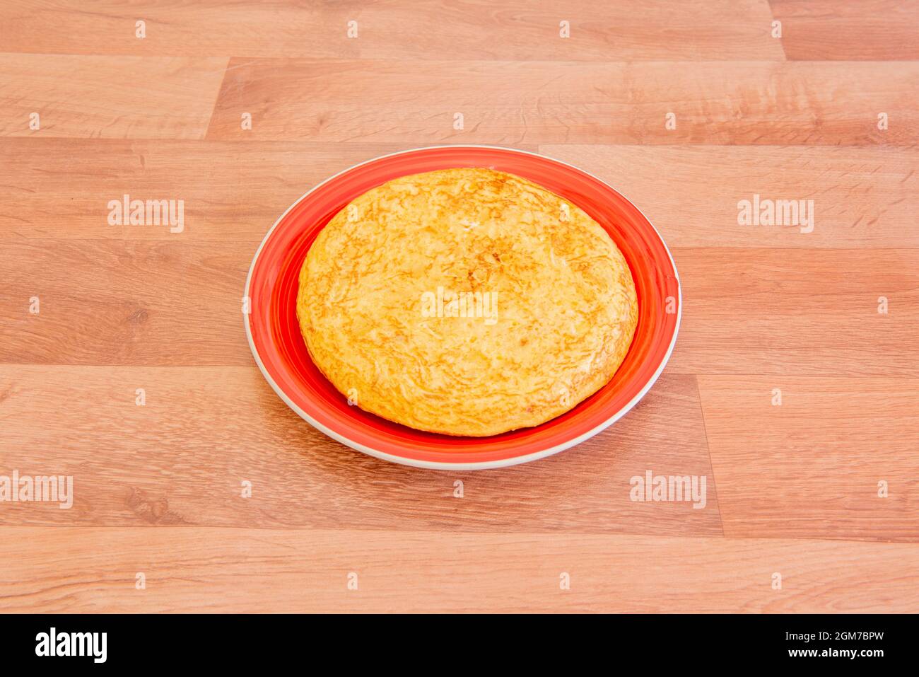 Spanisches Kartoffelomelett mit dem Aroma von Boletus auf einem roten Teller und einem Holztisch. Stockfoto