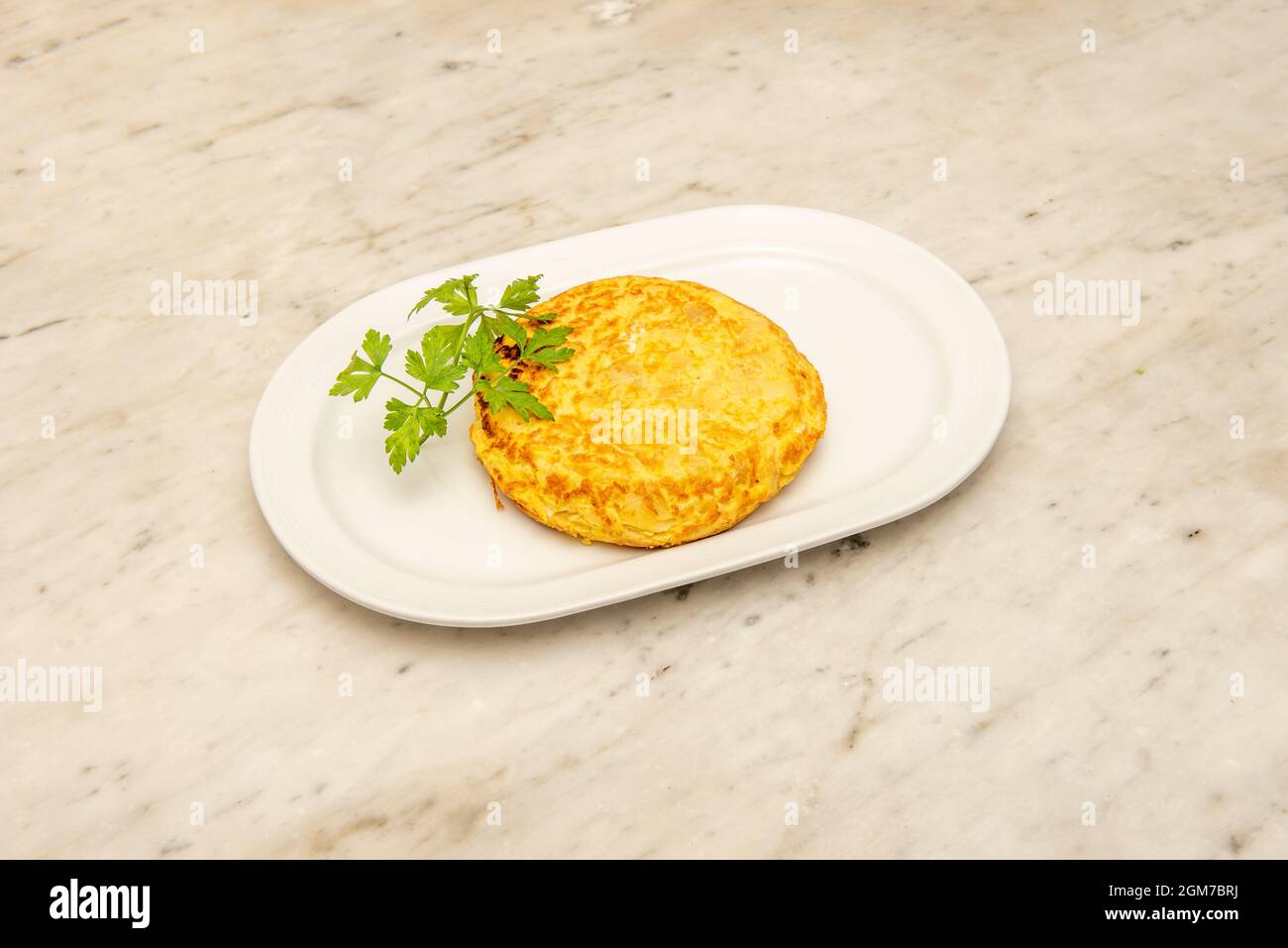 Spanisches Zucchini-Omelett, garniert mit Petersilie auf einem weißen Marmortisch Stockfoto