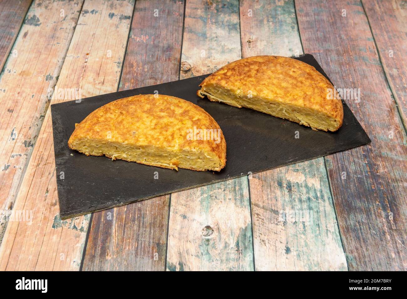 Spanisches Kartoffelomelett halbierte sich auf schwarzem Schieferteller und Holztisch Stockfoto
