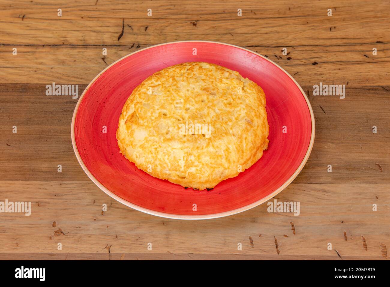 Kleines Kartoffelomelett auf einem roten Teller auf einem Holztisch Stockfoto