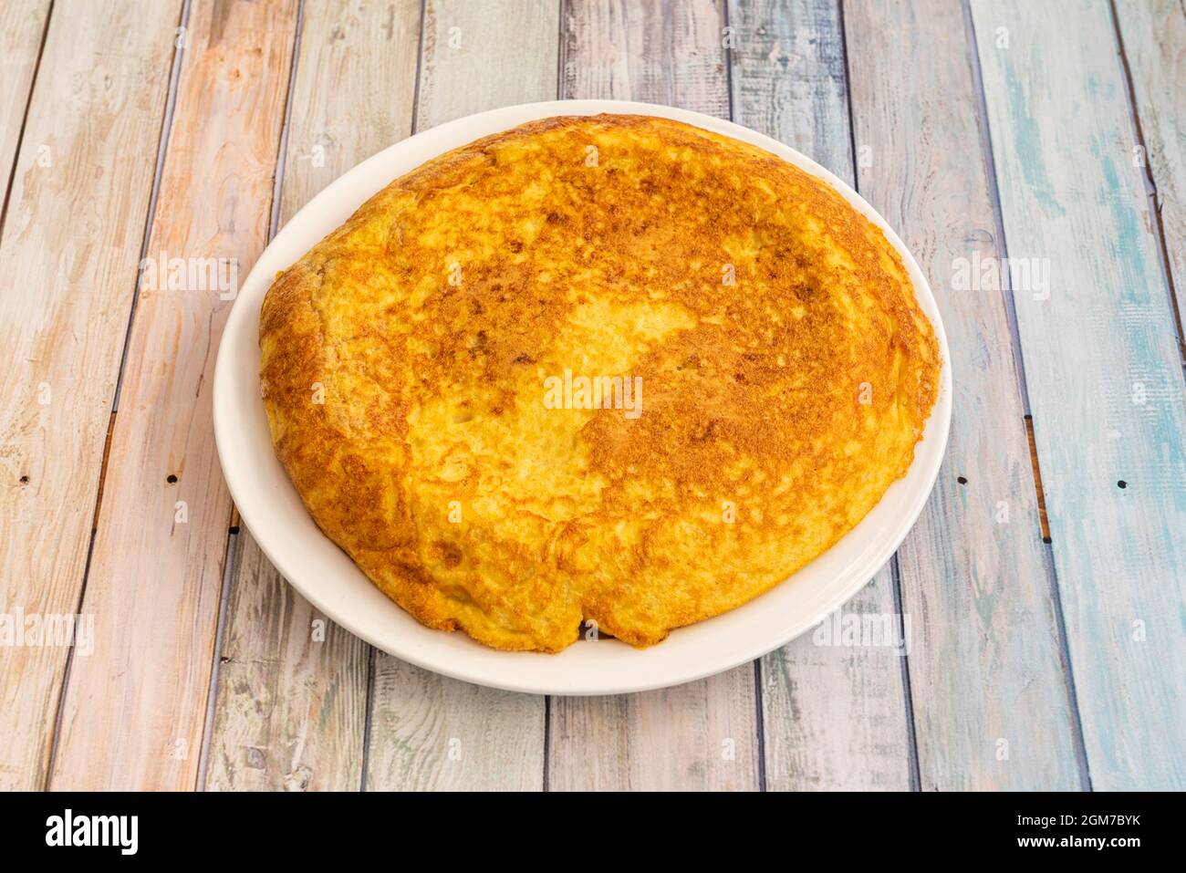 Spanisches Omelett, das in einem Tapas-Restaurant mit hellen Holztischen auf weißem Teller zubereitet wird Stockfoto