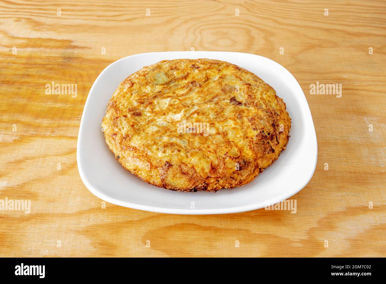 Beliebtes spanisches Kochrezept für spanisches Omelett auf weißem Teller und Kiefernholztisch Stockfoto