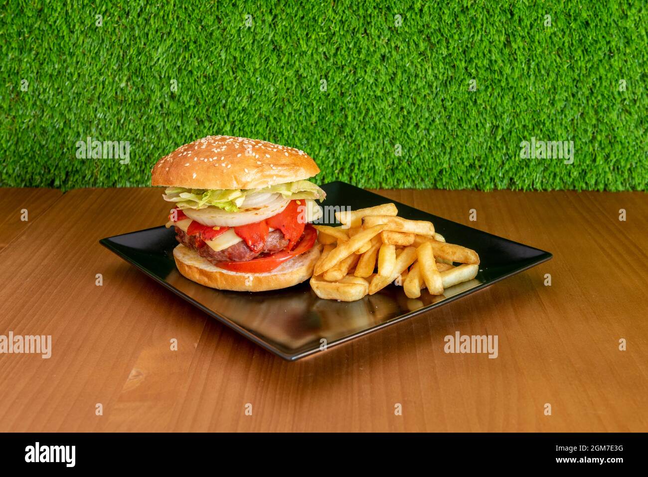 Schweineburger mit Käse, Piquillo-Paprika, Tomatenscheiben, weißen Zwiebelringen, Eisbergsalat und einer Portion Pommes Frites Stockfoto