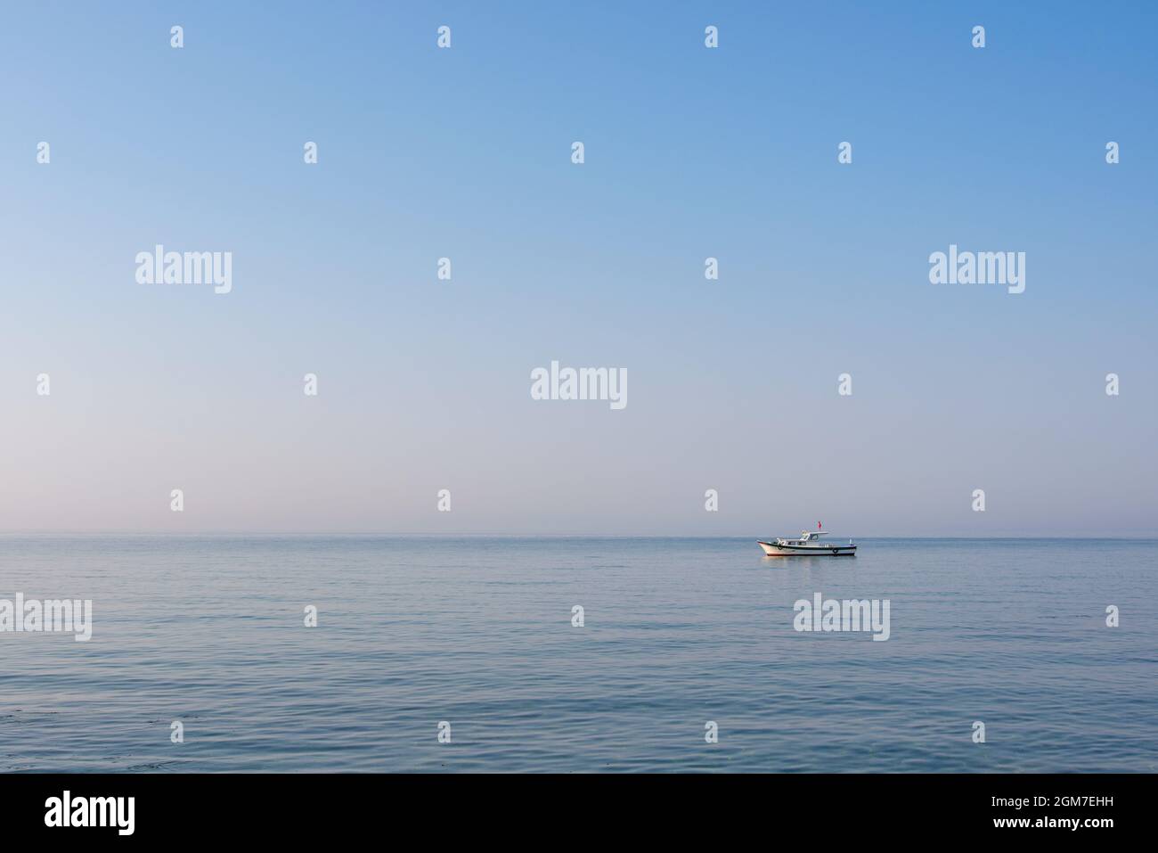 An einem ruhigen Tag bei Sonnenaufgang liegt ein kleines Motorboot vor der Küste einer türkischen Insel in der Ägäis Stockfoto