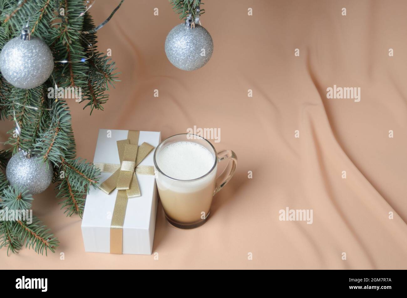 Eine Neujahrskomposition aus Zweigen eines Weihnachtsbaums, verziert mit silbernen Kugeln, einer Geschenkbox, einem Glaskrug mit Kaffee und Milch auf dem Backgr Stockfoto