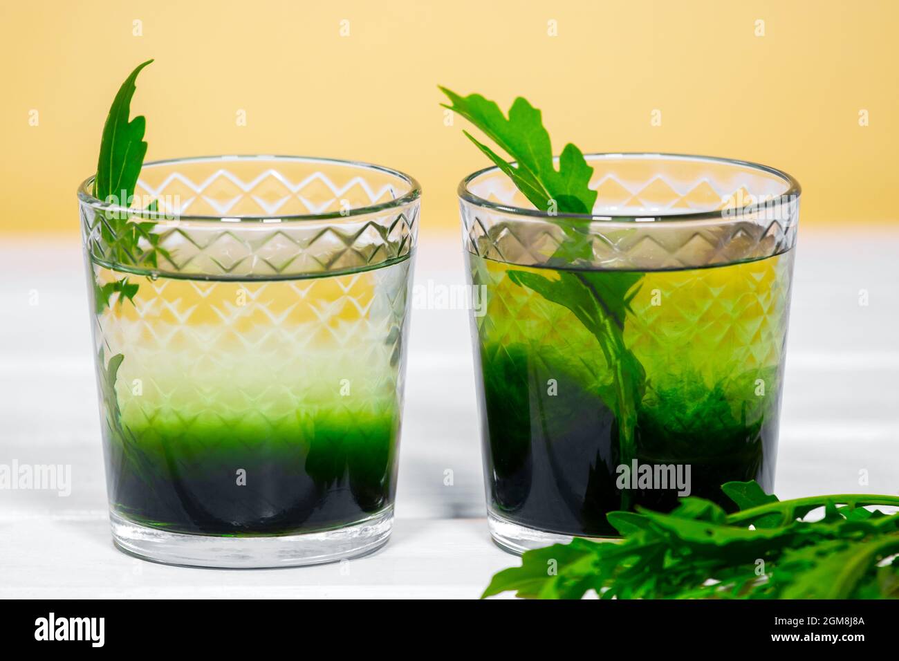 Grünes Chlorophyll oder Chlorella Getränk im Glas mit Wasser auf weißem Tisch, oranger Hintergrund. Grüne Tropfen in klarem Wasser, Antioxidantien, Speisen und Getränke. Stockfoto