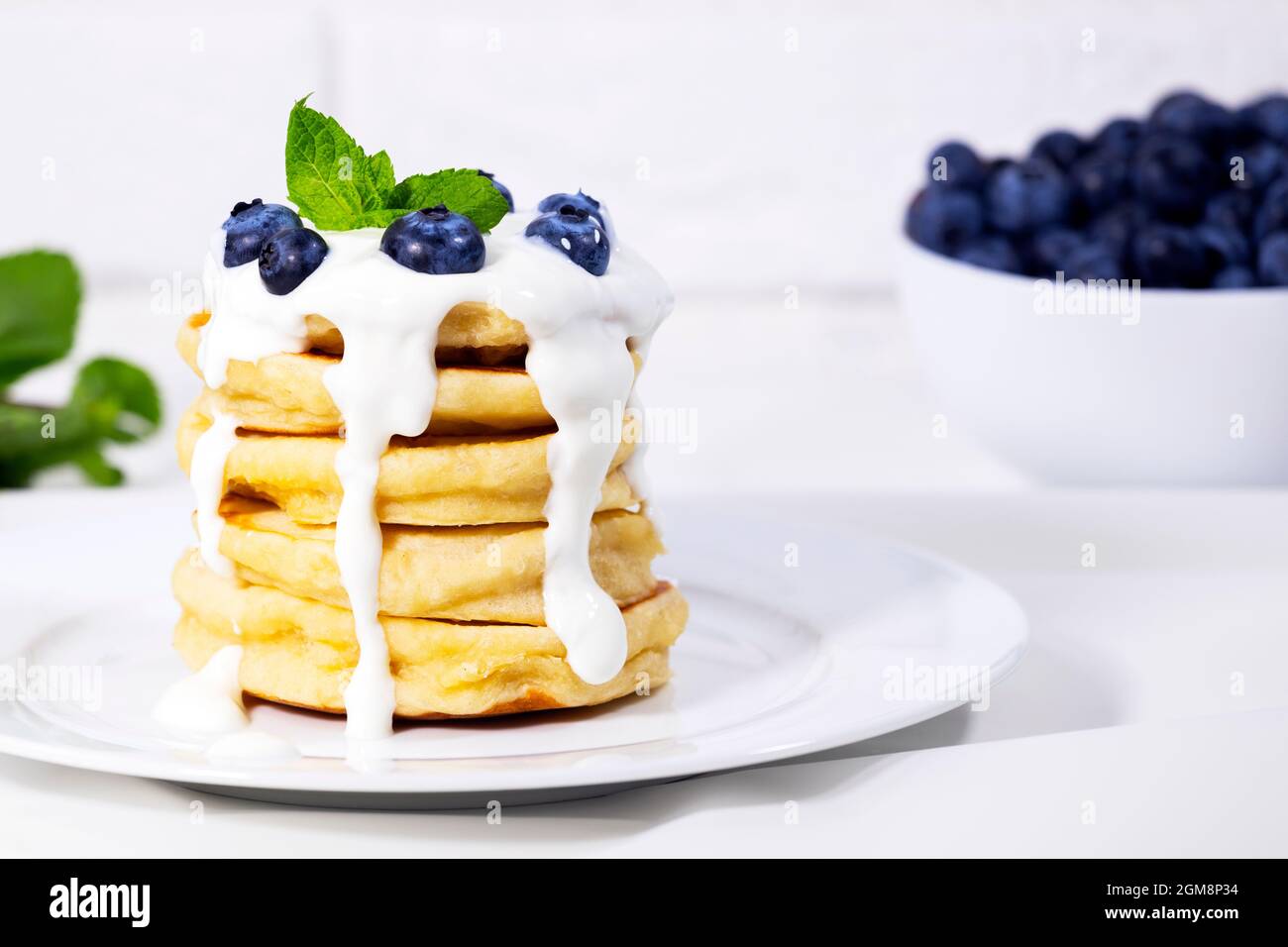 Heidelbeer-Pfannkuchen mit Joghurt und Minze auf weißem Hintergrund, traditionelles amerikanisches gesundes Frühstück, Copyspace, vertikale Auflösung Stockfoto