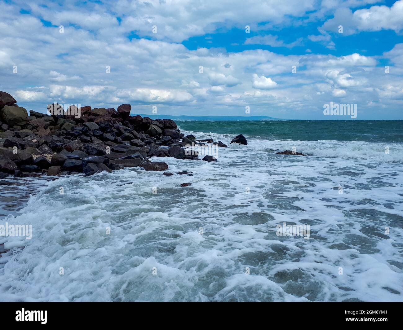 Schwarze Felsen und Wellen an der Schwarzmeerküste vor dramatischem Himmel in Pomorie, Burgas Bay, Bulgarien. Stockfoto