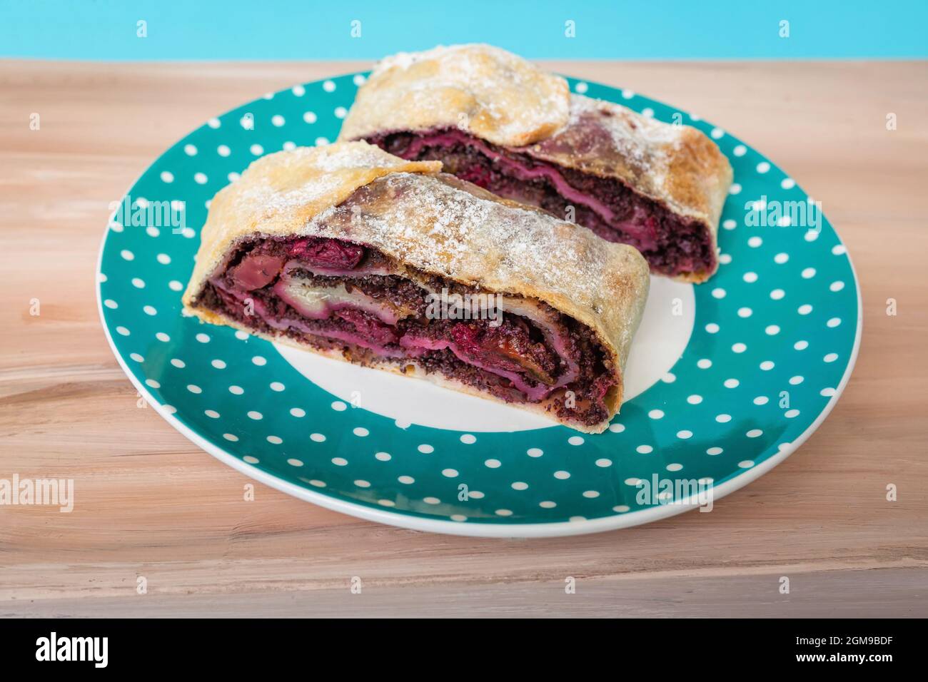 Hausgemachtes Fruchtdessert aus Pflaumen, Sauerkirschen und Mohn auf weißem und türkisfarbenem Teller auf braunem Holztisch. Stockfoto