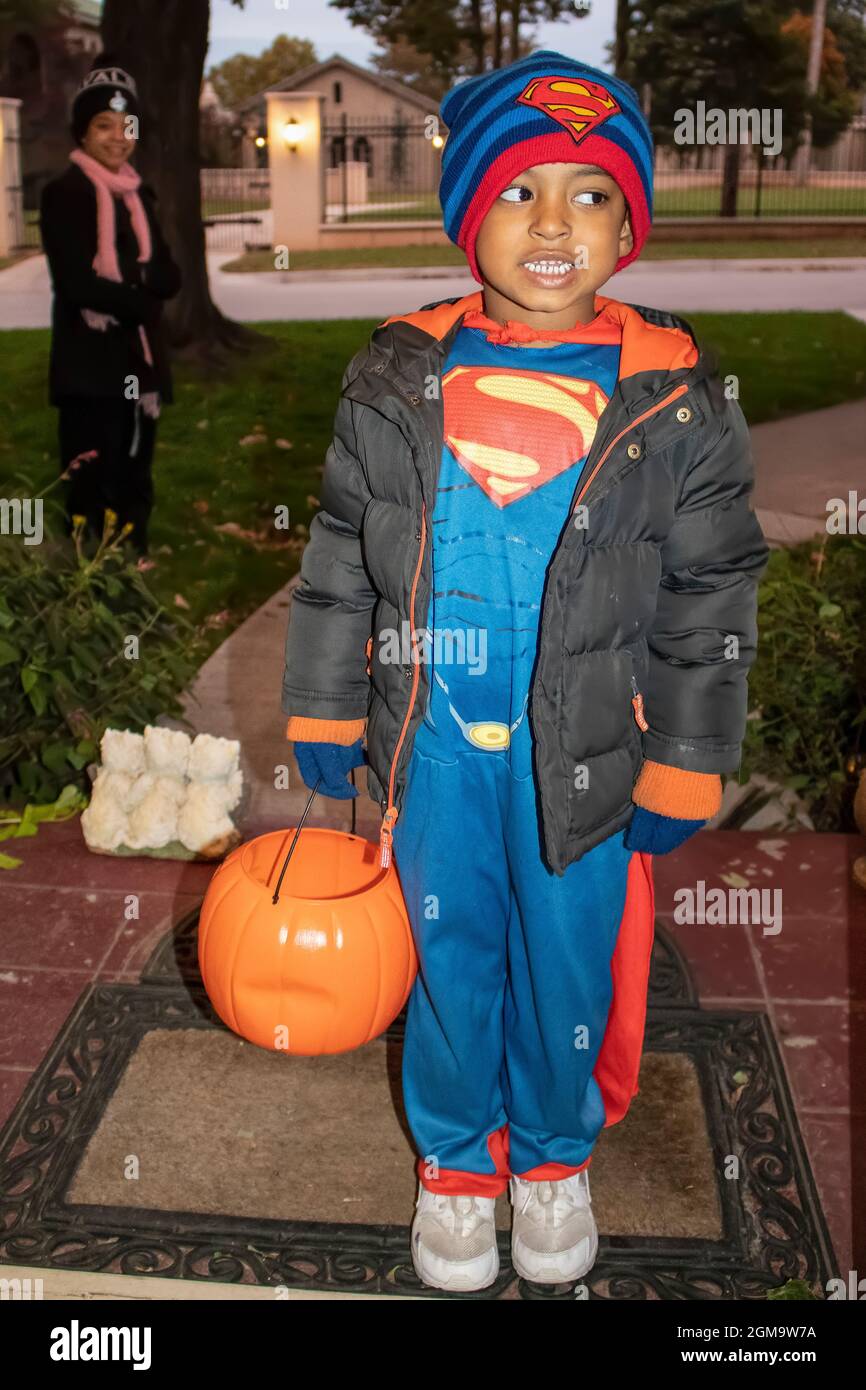 10-31-2017 Tulsa USA - junger schwarzer Junge, gekleidet in Superman-Kostüm mit Kürbis-Süßigkeitenkorb und Jacke, die vor der Tür steht, um mit der Mutter zu behandeln Stockfoto