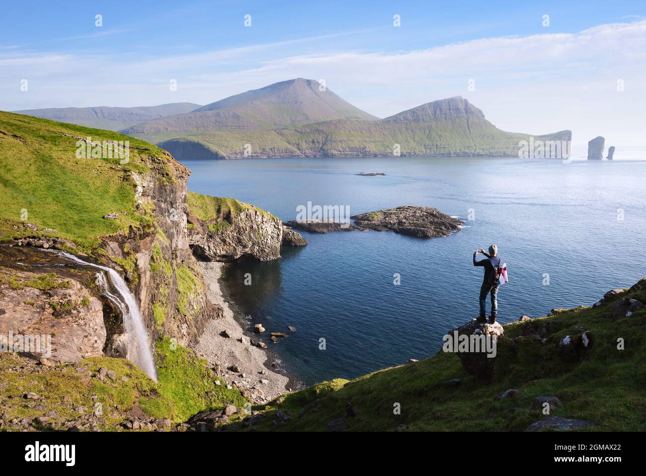 Der Typ macht Fotos am Telefon Skardsafossur Wasserfall und Drangarnir Meer Stapel Blick auf Färöer-Inseln Stockfoto