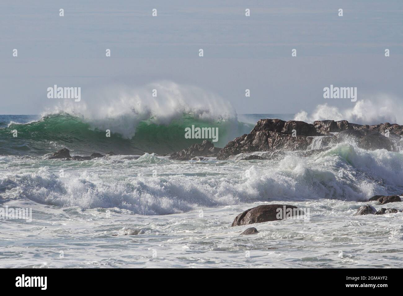 An einem sonnigen Tag brechen Wellen an einem Strand der nordportugiesischen Küste mit Spray. Stockfoto