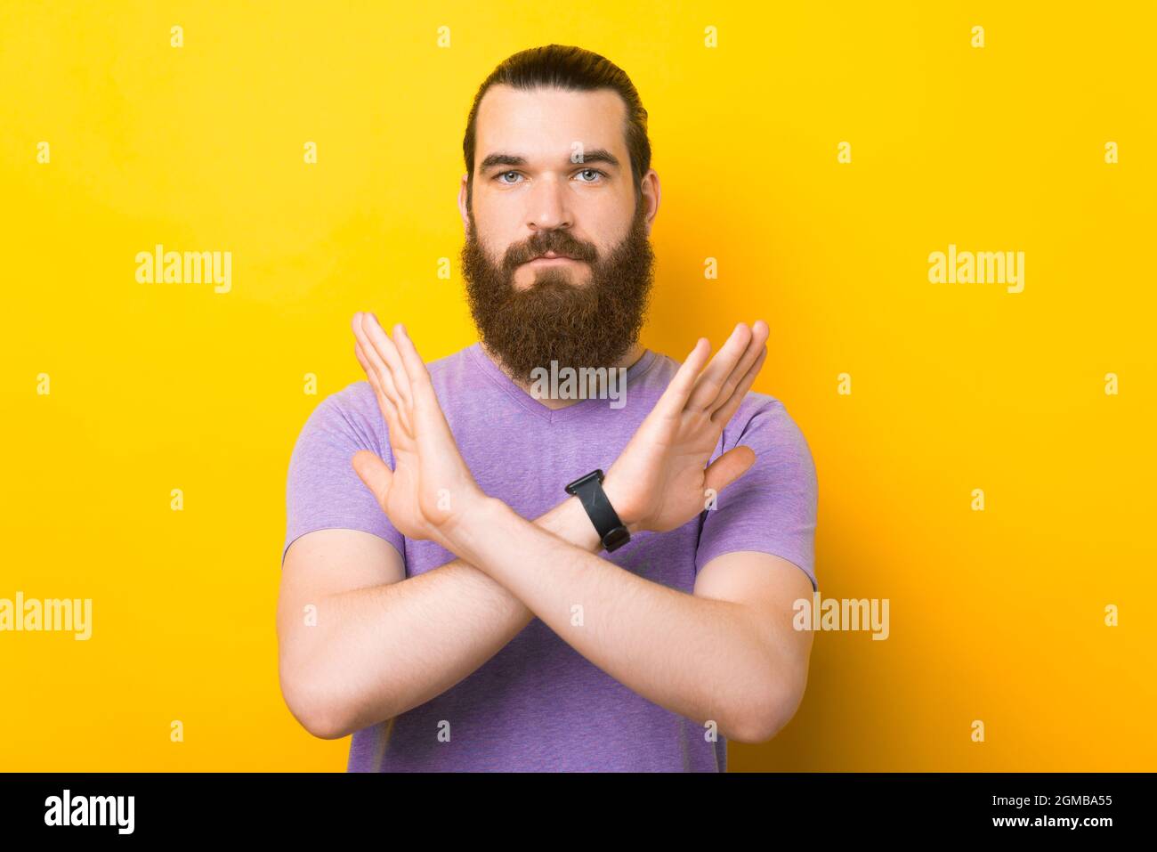 Ernsthafter Mann kreuzt die Hände, um die No-Geste auf gelbem Hintergrund zu bilden. Stockfoto