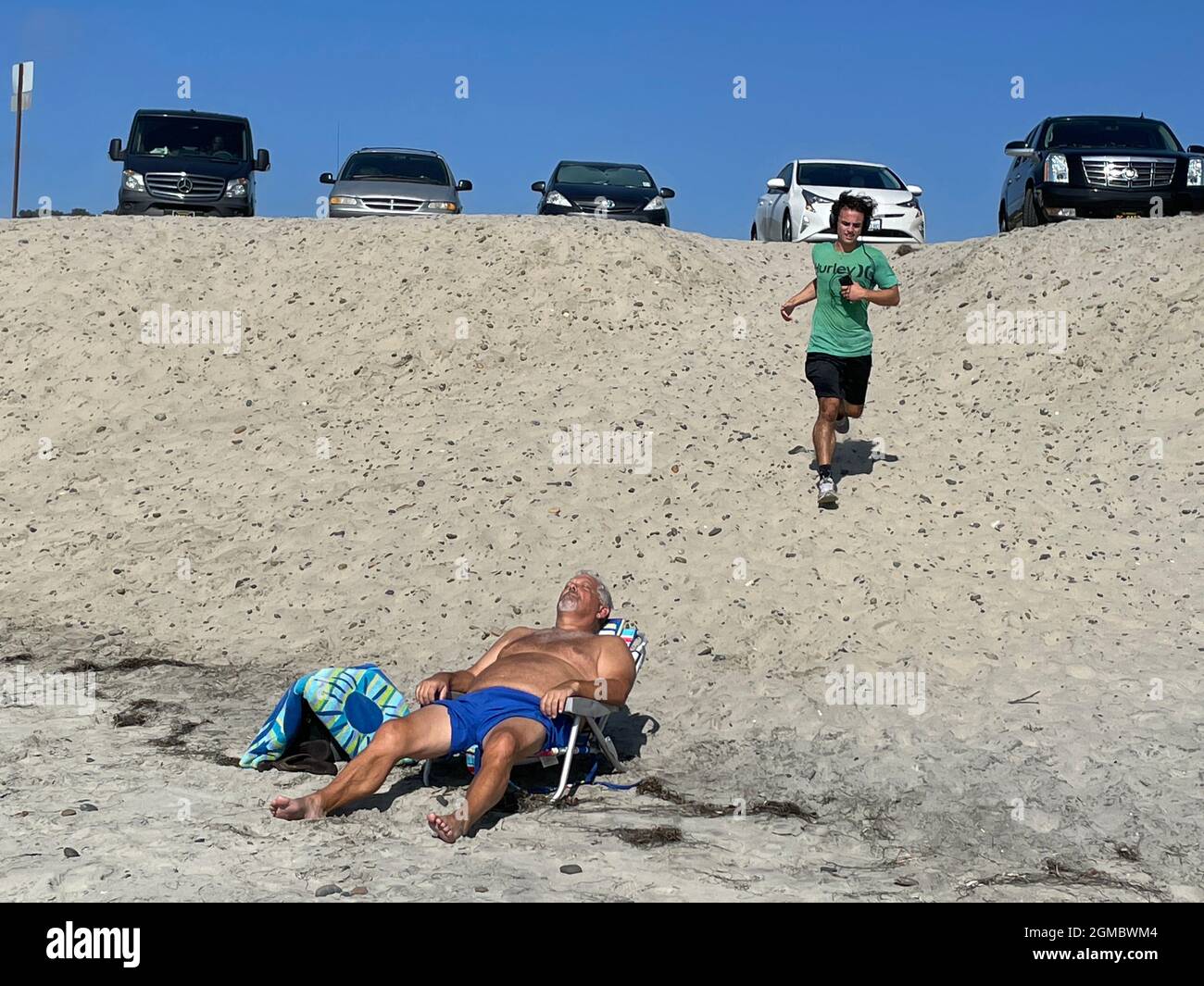 Mann, der sich in einem Liegestuhl ausruhte, mit Läufer und Autos, die am Strand in Del Mar, CA, geparkt waren Stockfoto
