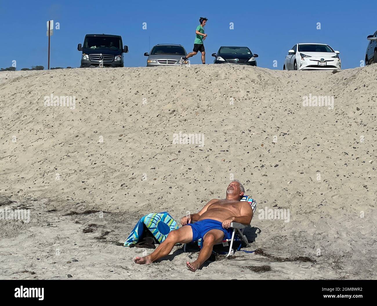 Mann, der sich in einem Liegestuhl ausruhte und Autos hinter dem Strand in Del Mar, CA, parkten Stockfoto