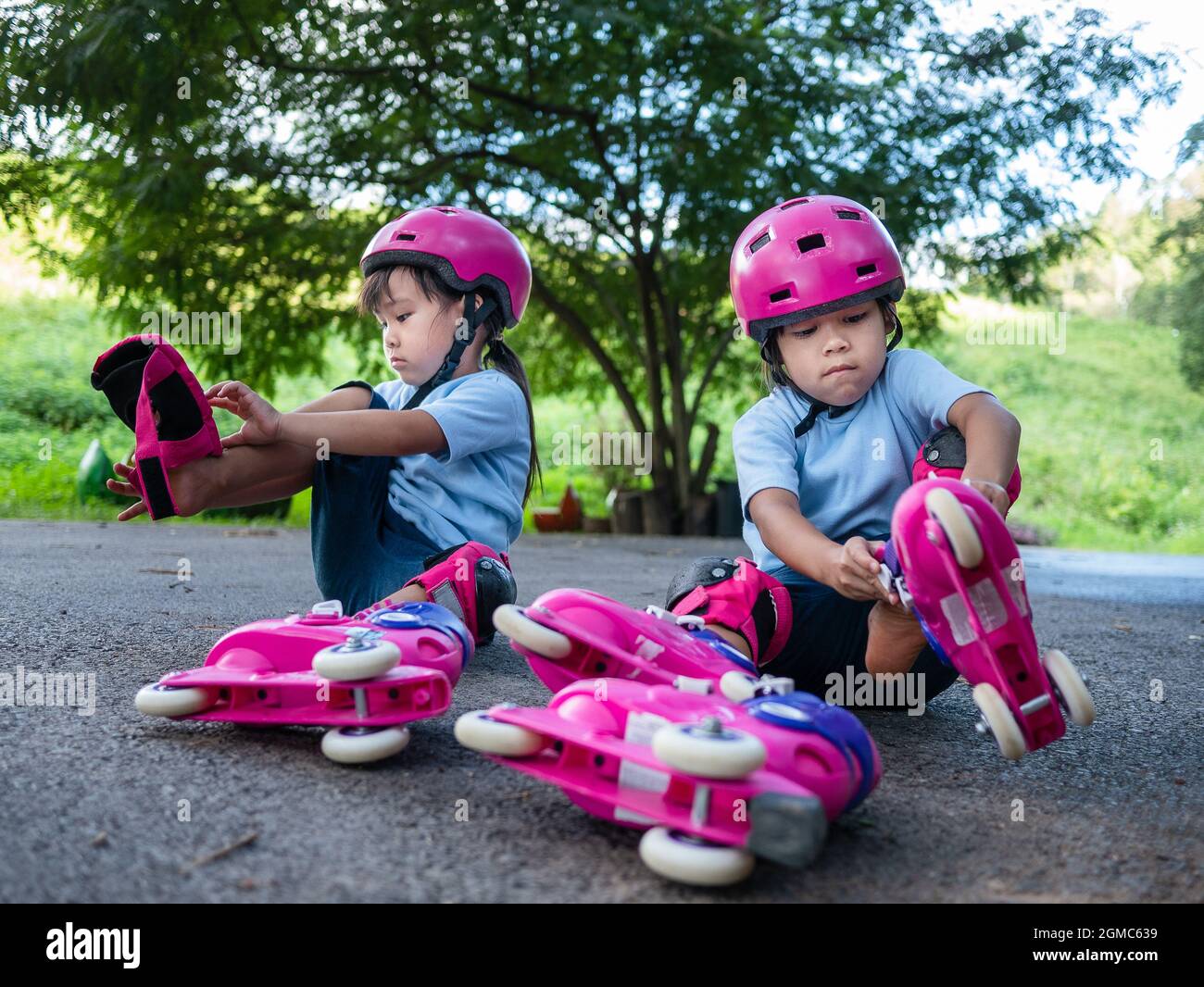 Zwei Geschwisterschwestern mit Schutzpolstern und Schutzhelm üben auf der Straße im Park das Rollschuhlaufen. Aktiver Outdoor-Sport für Kinder. Stockfoto