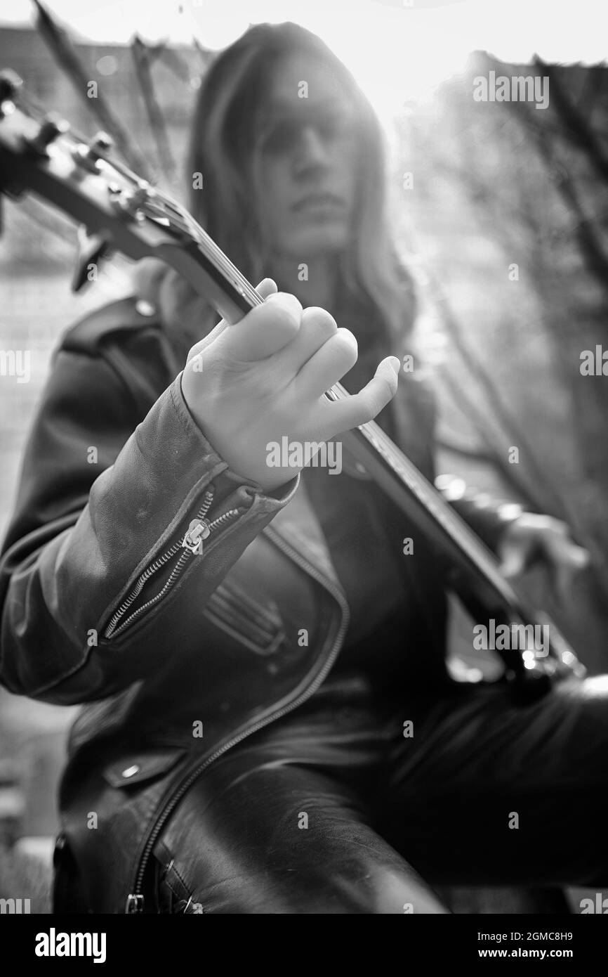 Rock Gitarrist auf die Schritte. Ein Musiker mit einer Bassgitarre in einer Lederkombi. Metalist mit einer Gitarre auf dem Hintergrund der industriellen Schritt. Stockfoto