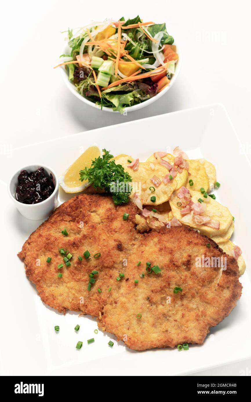 deutsche panierte Schweinefleischschnitzel mit Speck Bratkartoffeln Preiselbeersauce und Salat auf weißem Studiohintergrund Stockfoto