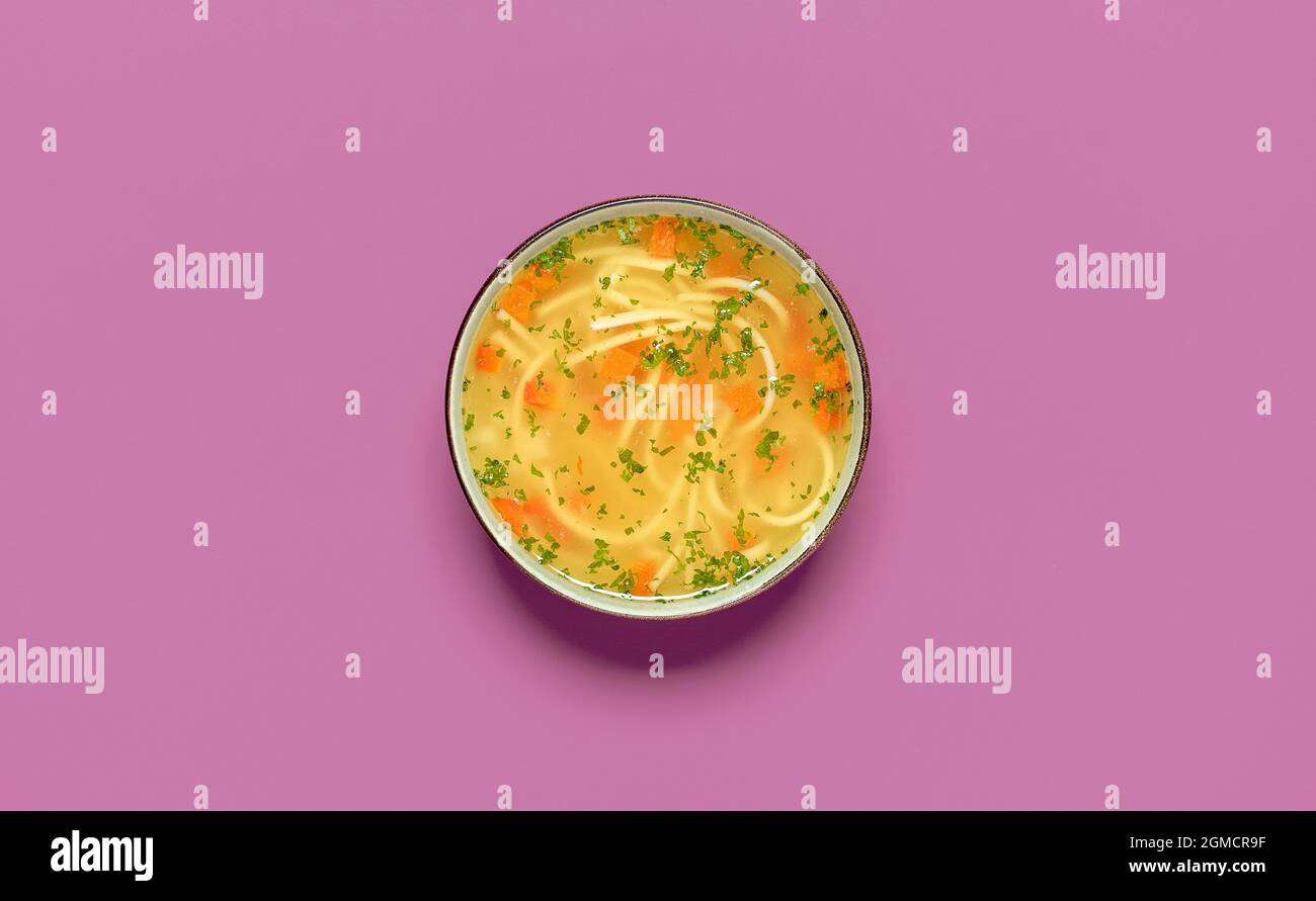 Draufsicht mit einer Schüssel Hühnersuppe isoliert auf einem violetten Hintergrund. Köstliche hausgemachte Hühnersuppe mit Gemüse und Nudeln. Stockfoto