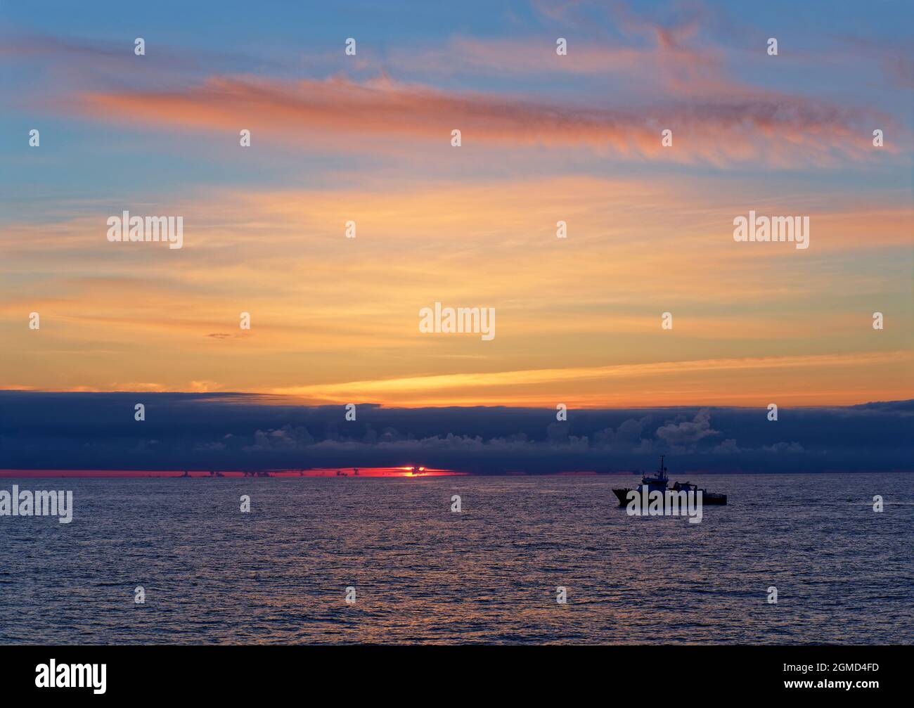 Sonnenaufgang über dem Alvheim-Feld in der norwegischen Nordsee mit einem Seismic Escort-Schiff, das gegen die aufgehende Sonne silhouettiert wurde Stockfoto