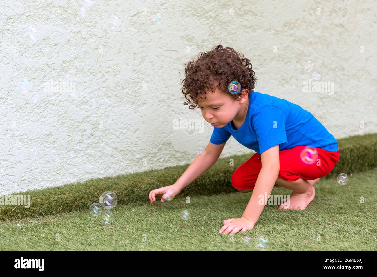 Schöner 4-5-jähriger kaukasischer Junge mit lockigem Haar in seinem Hinterhof, der mit Seifenblasen spielt Stockfoto