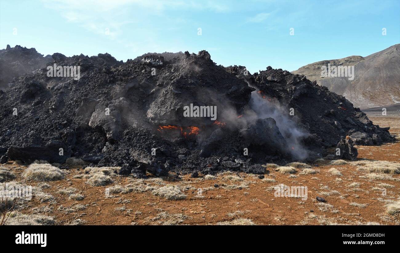 Lavastrom am Fagradalsfjall, Island. Glühende orange Lava sichtbar, innerhalb der schwarzen Lavakruste. Grüne und braune Vegetation im Vordergrund. Stockfoto