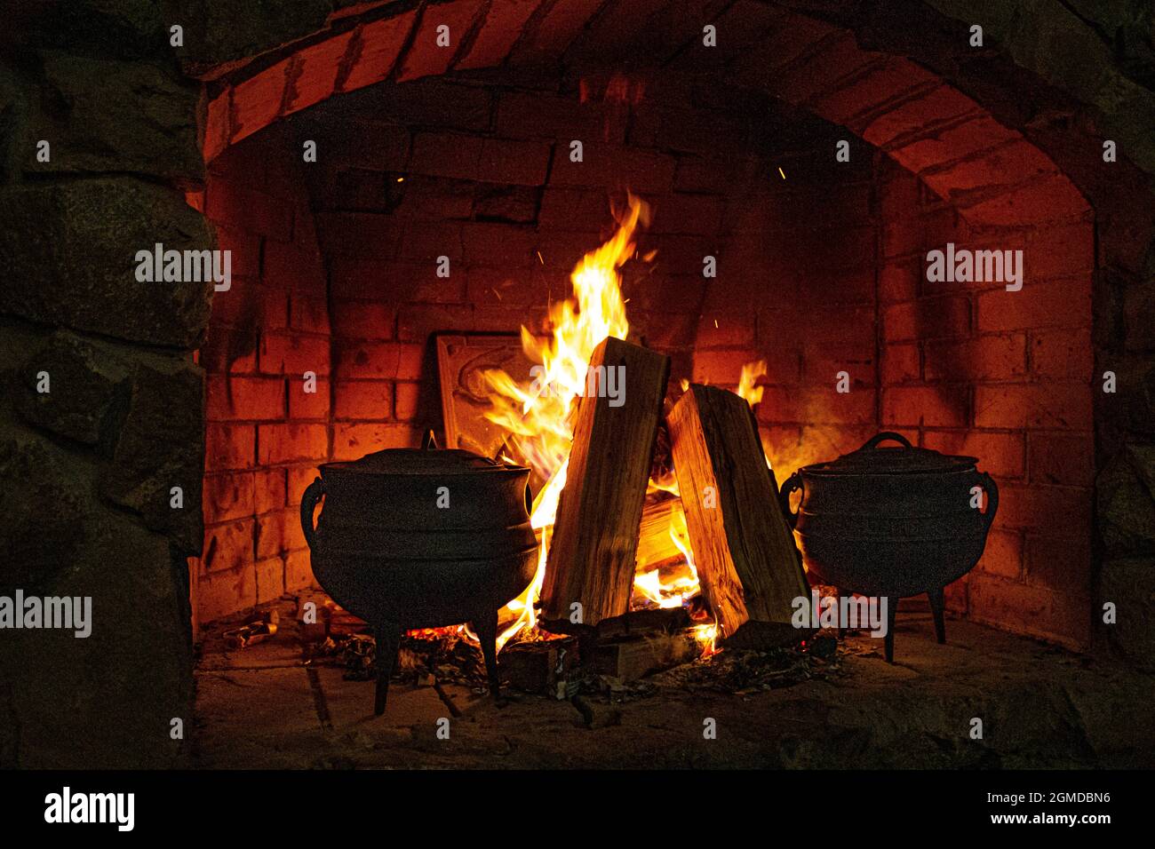 Das Essen wird im Kamin zubereitet. Ausbreitung des Feuers. Lagerfeuer und Brennholz. Feuer. Gusseiserne Auflaufform im Ofen. Meldet sich im Feuer. Feuer und Funken. Stockfoto