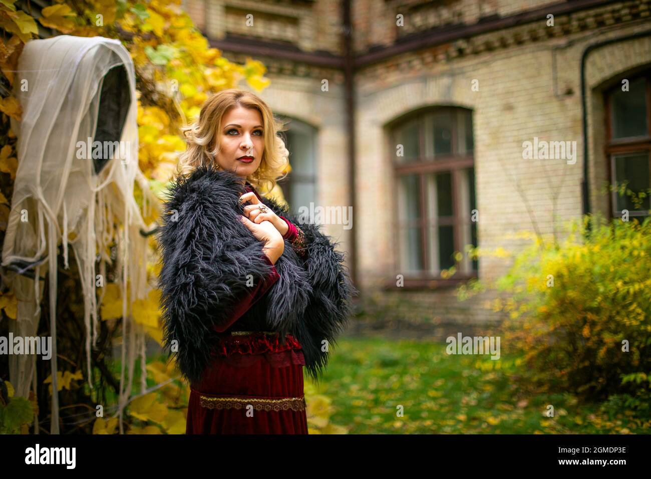 Schöne Frau in einem Hexenkostüm steht auf einem Hintergrund von Geistern. Stilisiertes Halloween-Dekor. Stockfoto