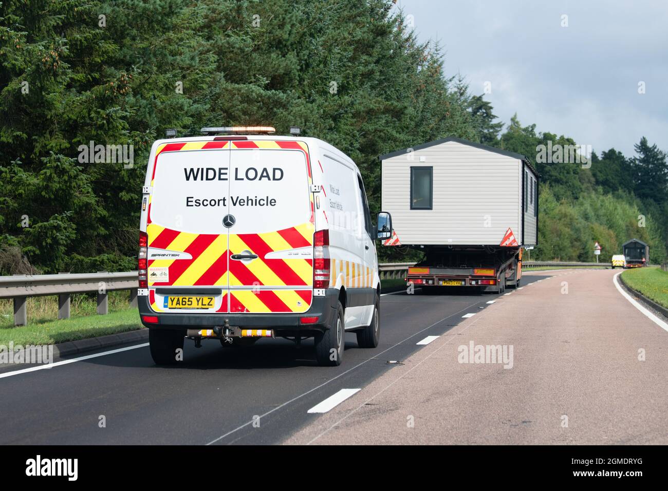Breitlast-Begleitfahrzeug, das hinter einem statischen Wohnwagen-Wohnmobil unterwegs ist und auf der Straße A9, Schottland, Großbritannien, auf einem Lastkraftwagen transportiert wird Stockfoto