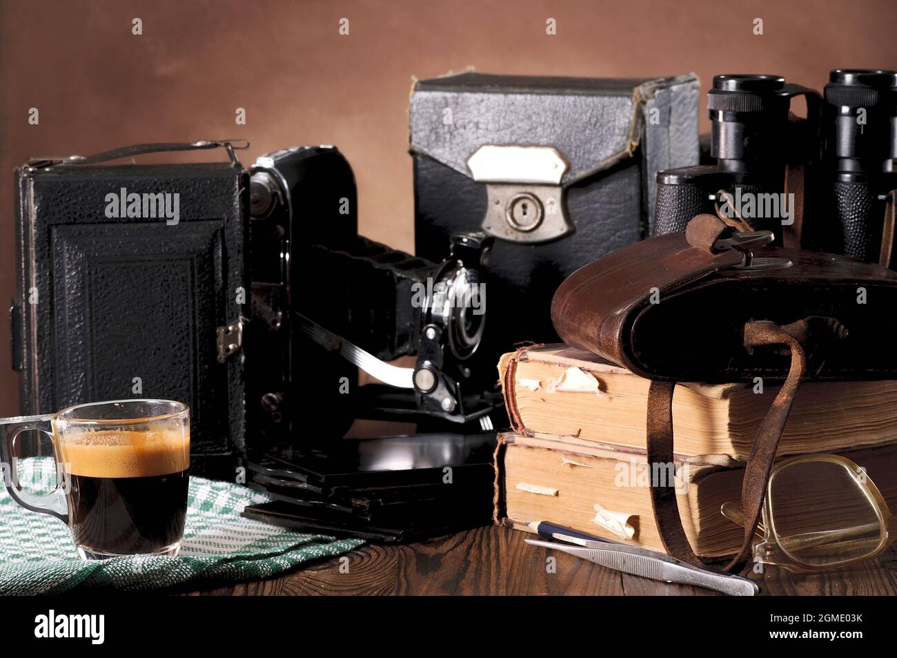 Stapel alter Bücher, Ferngläser, Vintage-Kamera, ausgefranste Ledertaschen auf einem Holztisch Stockfoto