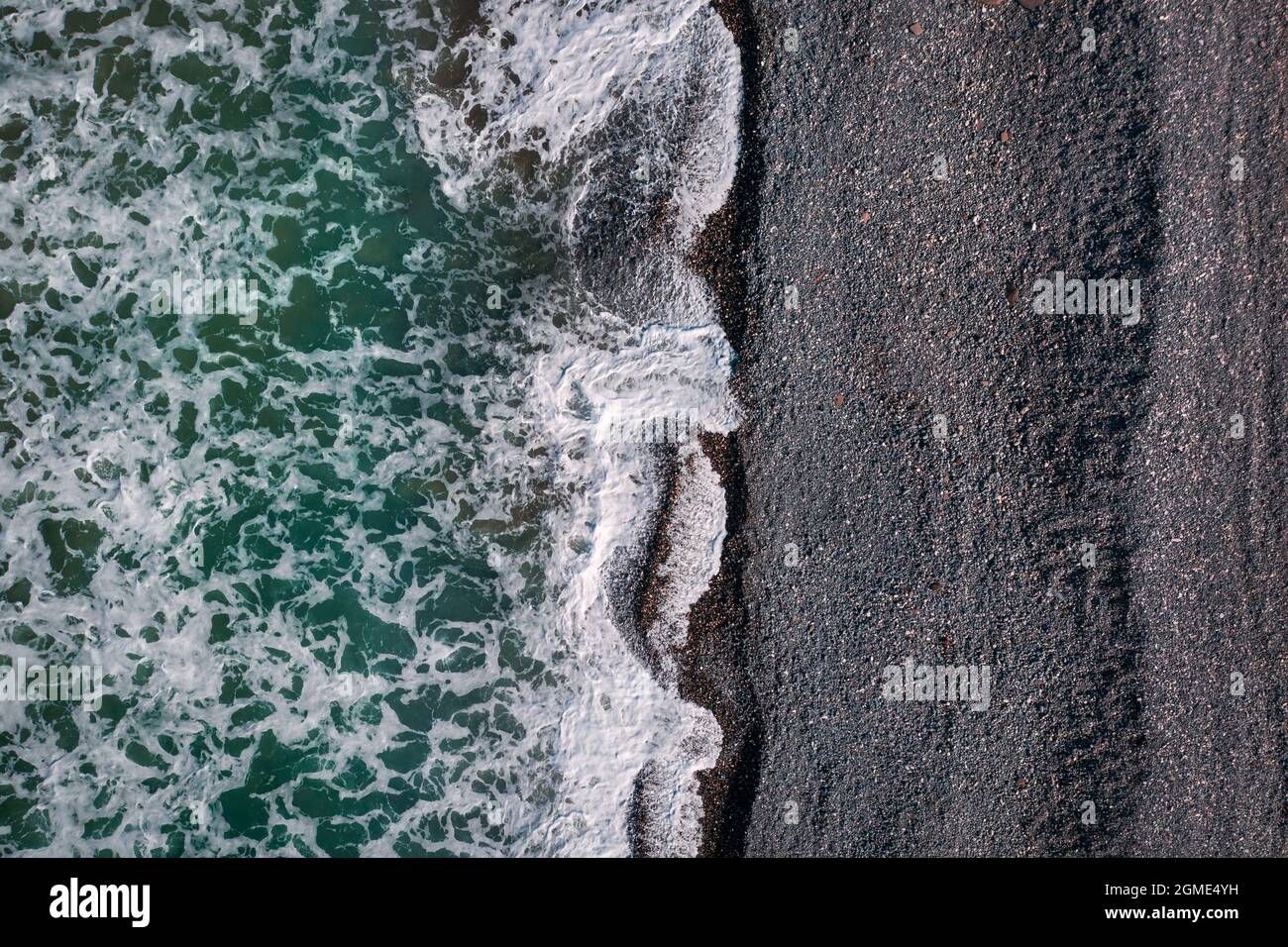 Grüne stürmische Wellen mit Meeresschaum, der am schwarzen Sandstrand bricht, Blick auf die Meeresstruktur direkt darüber Stockfoto