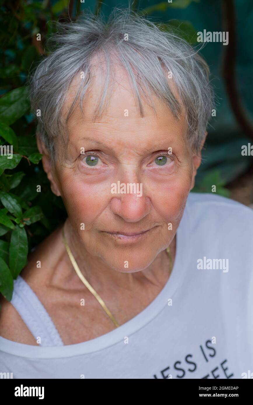 Reife Frau, die die Kamera anschaut. Ältere Dame lächelt in ihrem Garten. Nahaufnahme glückliches weibliches Gesicht. Porträt eines weiblichen Models, das im Freien vor der Kamera posiert Stockfoto
