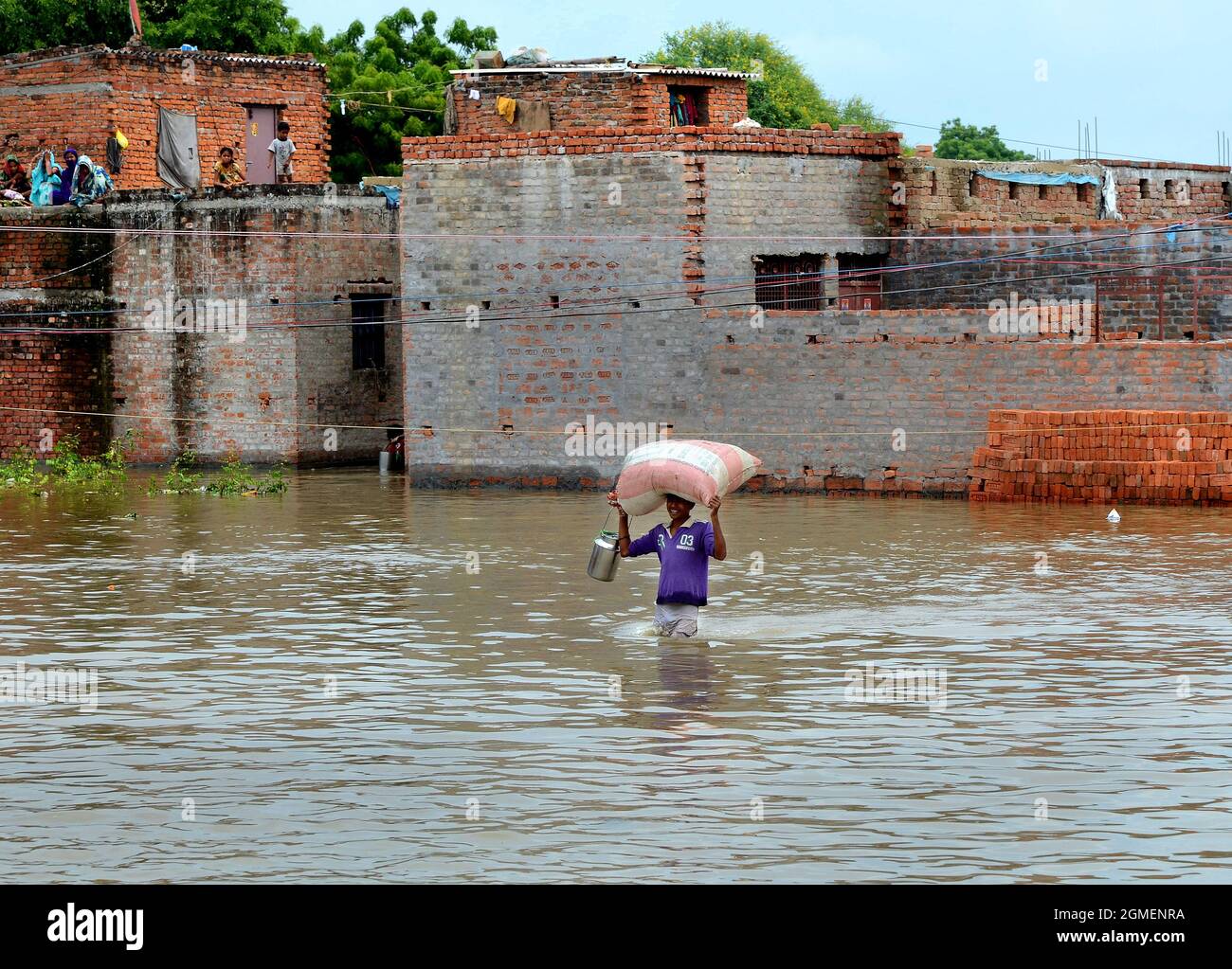 Der kleine, abgelegene Dorfjunge des zerstörerischen Überschwemmungsgebiets hat es schwer, seinen großen Sack mit einem kleinen Trinkwasserbehälter in Varanasi in Indien zu schützen. Stockfoto