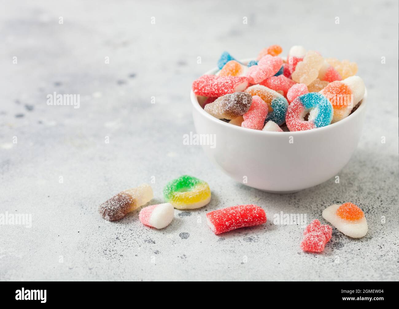 Bonbons mit Fruchtgeschmack und saurem Zucker in Keramikschale auf dem hellen Tisch Stockfoto