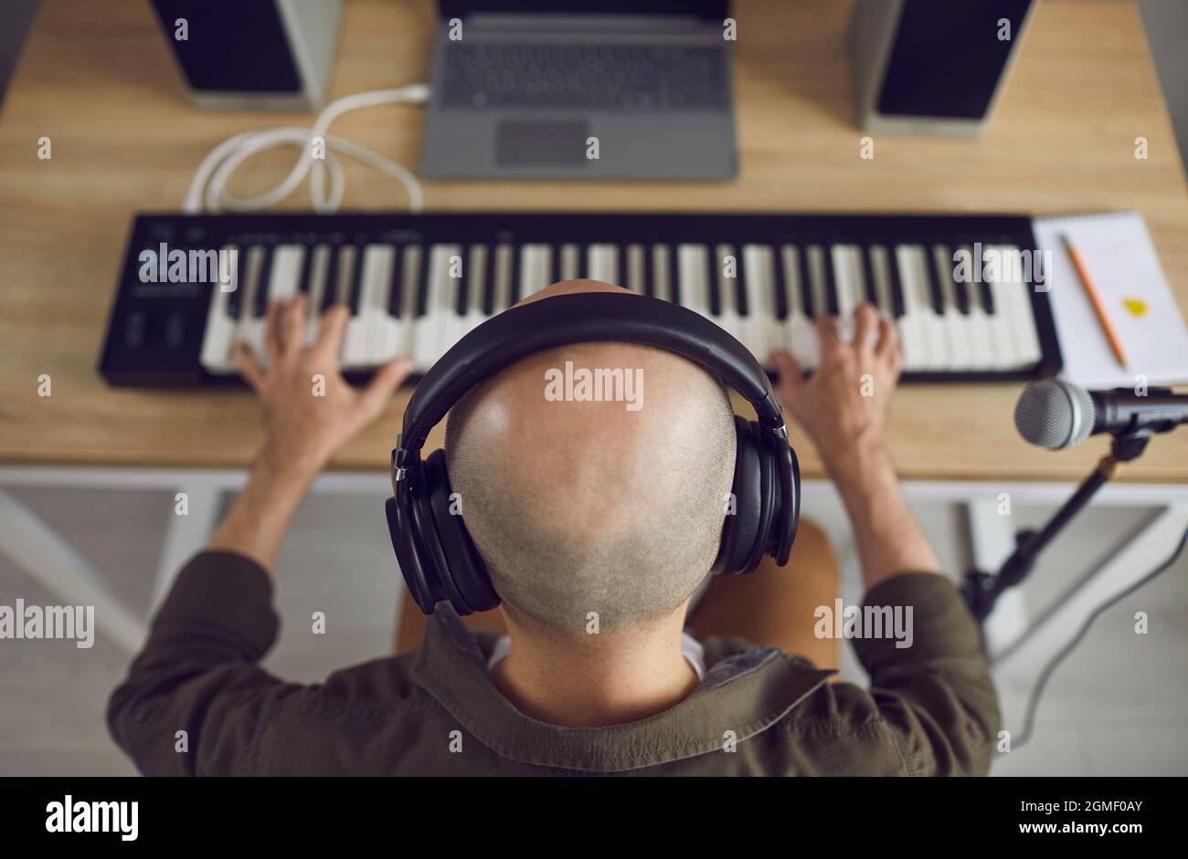 Kahlköpfiger Musiker mit Kopfhörern, der Musik aufnimmt, die er auf dem MIDI-Keyboard spielt Stockfoto