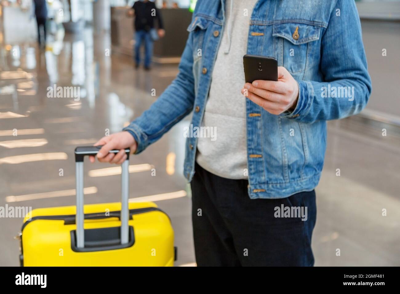 Mann, der am Flughafen ein Mobiltelefon benutzt. Stadtreisender in lässiger Kleidung hält Smartphone, Kerl SMS, während Koffer Gepäck im Flughafen Stockfoto