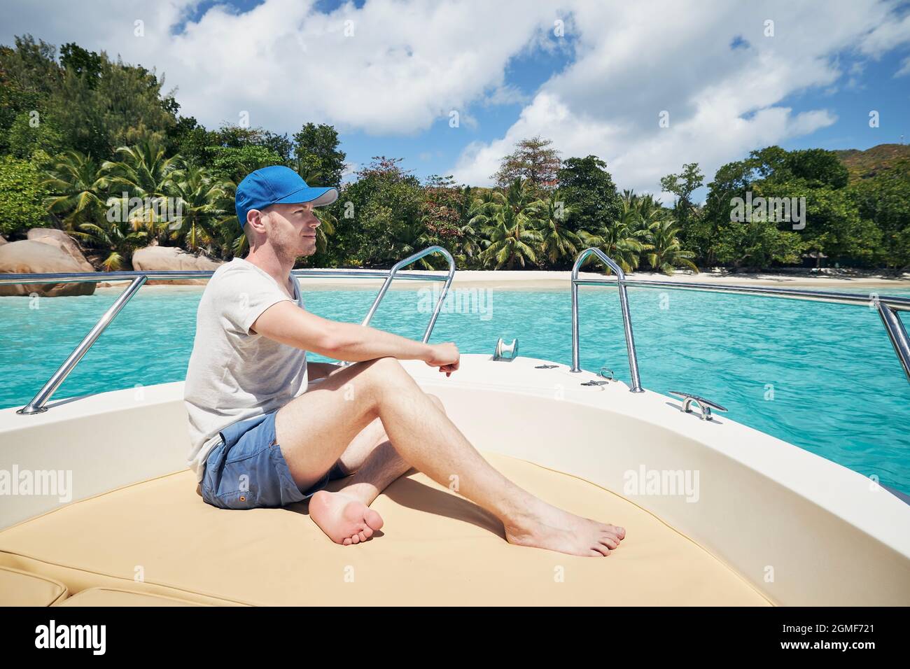 Mann, der sich auf dem Boot vor einem wunderschönen weißen Sandstrand mit Palmen ausruht. Anse Lazio, Seychellen. Stockfoto