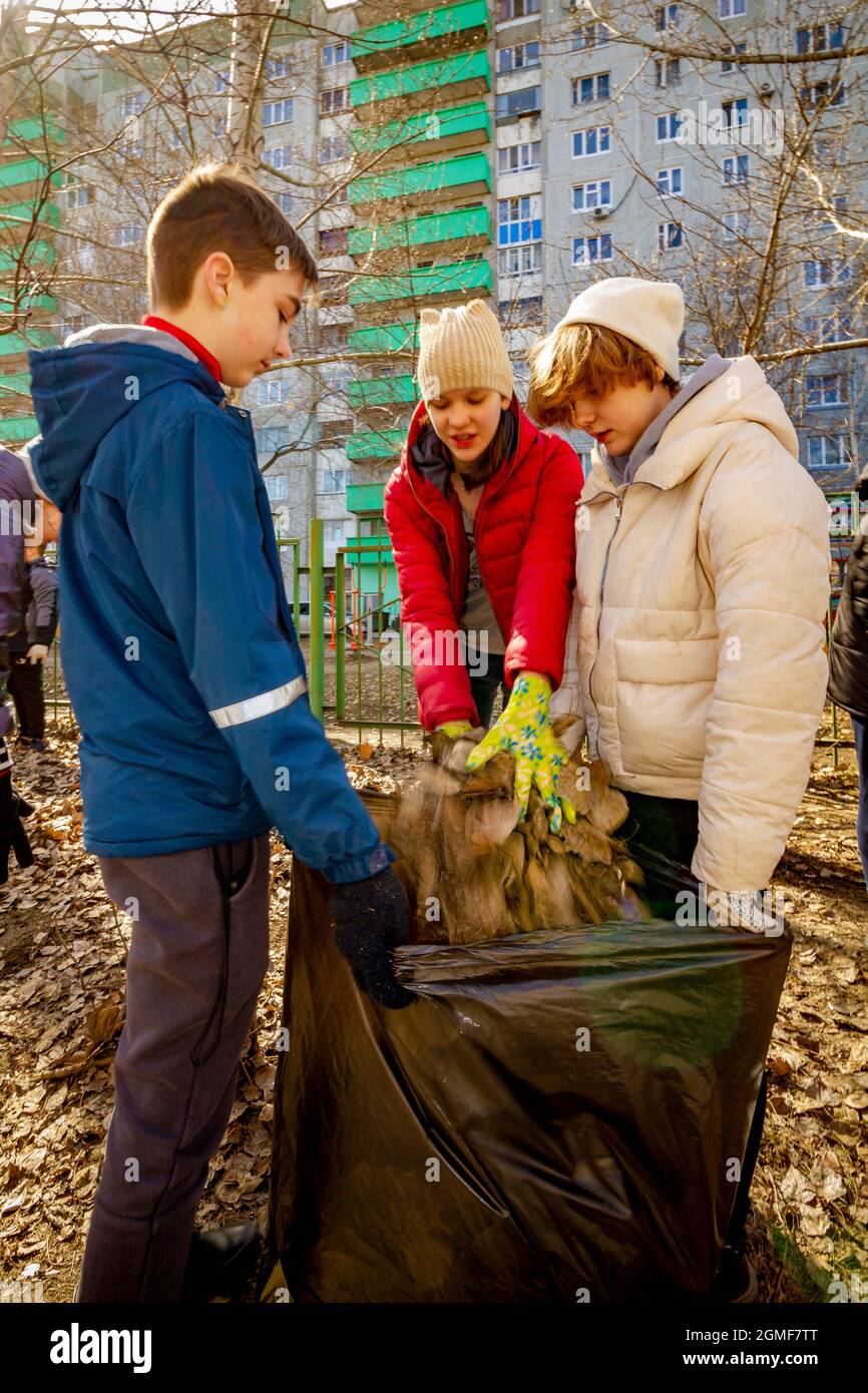 Omsk, Russland. 24. April 2021. Ein Schuljunge mit zwei Schülerinnen packt eine Tüte Laub. Traditionelle russische Veranstaltungen zur Vorbereitung der Schule Stockfoto