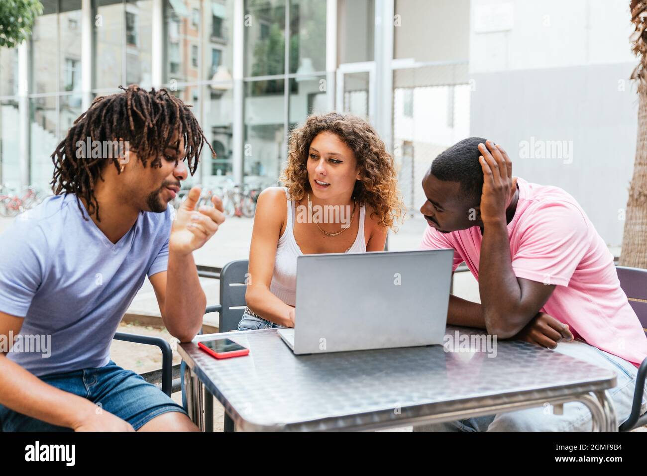 Junge kaukasische Frau, die draußen auf einem Tisch mit Laptop sitzt und einen lateinischen Mann anschaut. Konzept der Muti ethnischen Gruppe von Studenten Stockfoto