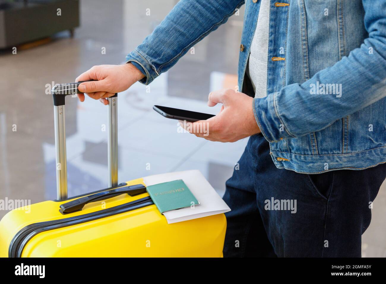 Smartphone in männlicher Hand am Flughafen. Urbane Reisende tragen legere hält Handy. Mann schreibt eine SMS, während er den Koffer im Gepäck hält Stockfoto