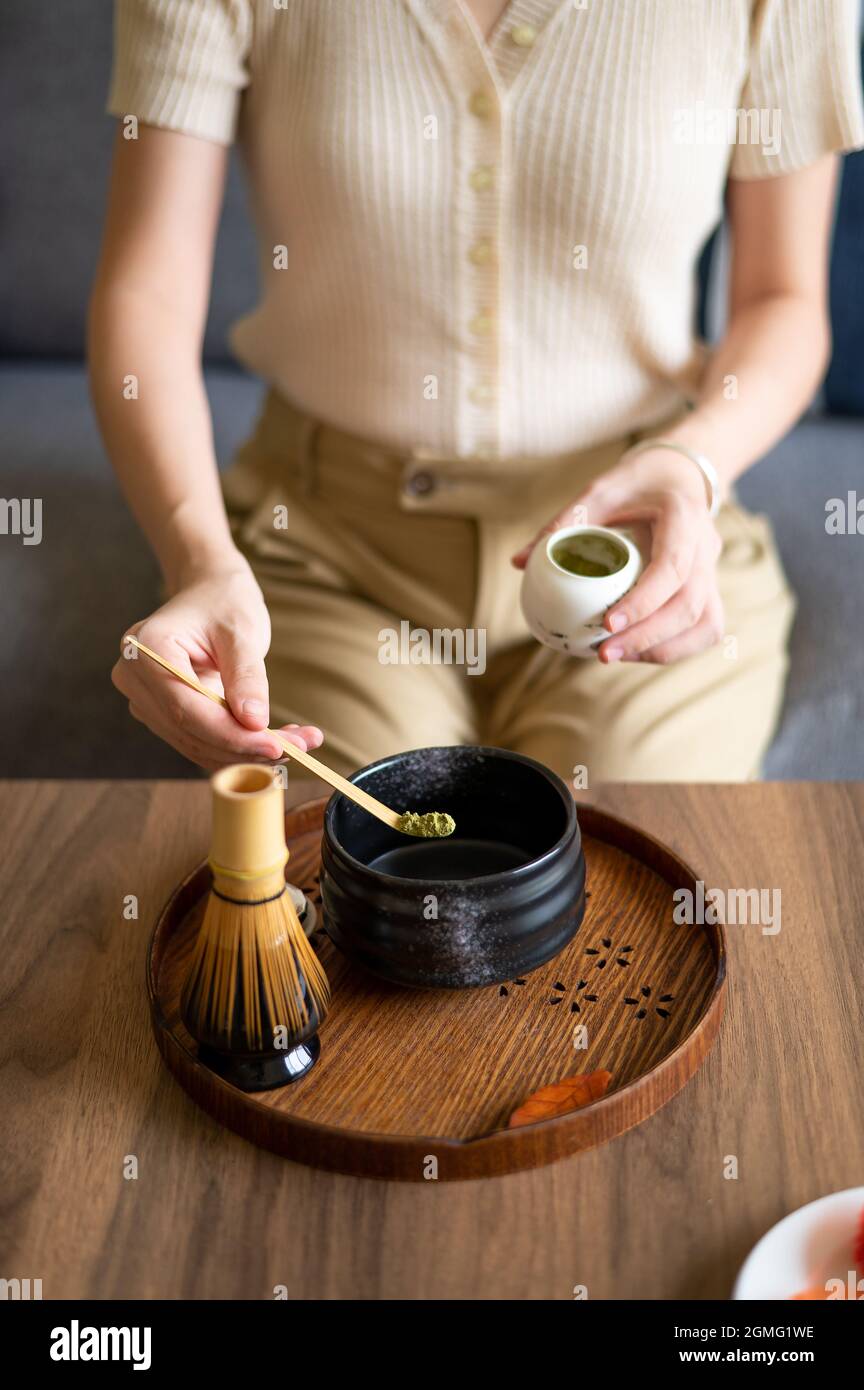 Frau, die zu Hause einen japanischen Matcha-Grüntee mit traditionellem Bambus-Set für Teezeremonien zubereitet, während sie zu Hause auf dem Sofa sitzt. Stockfoto