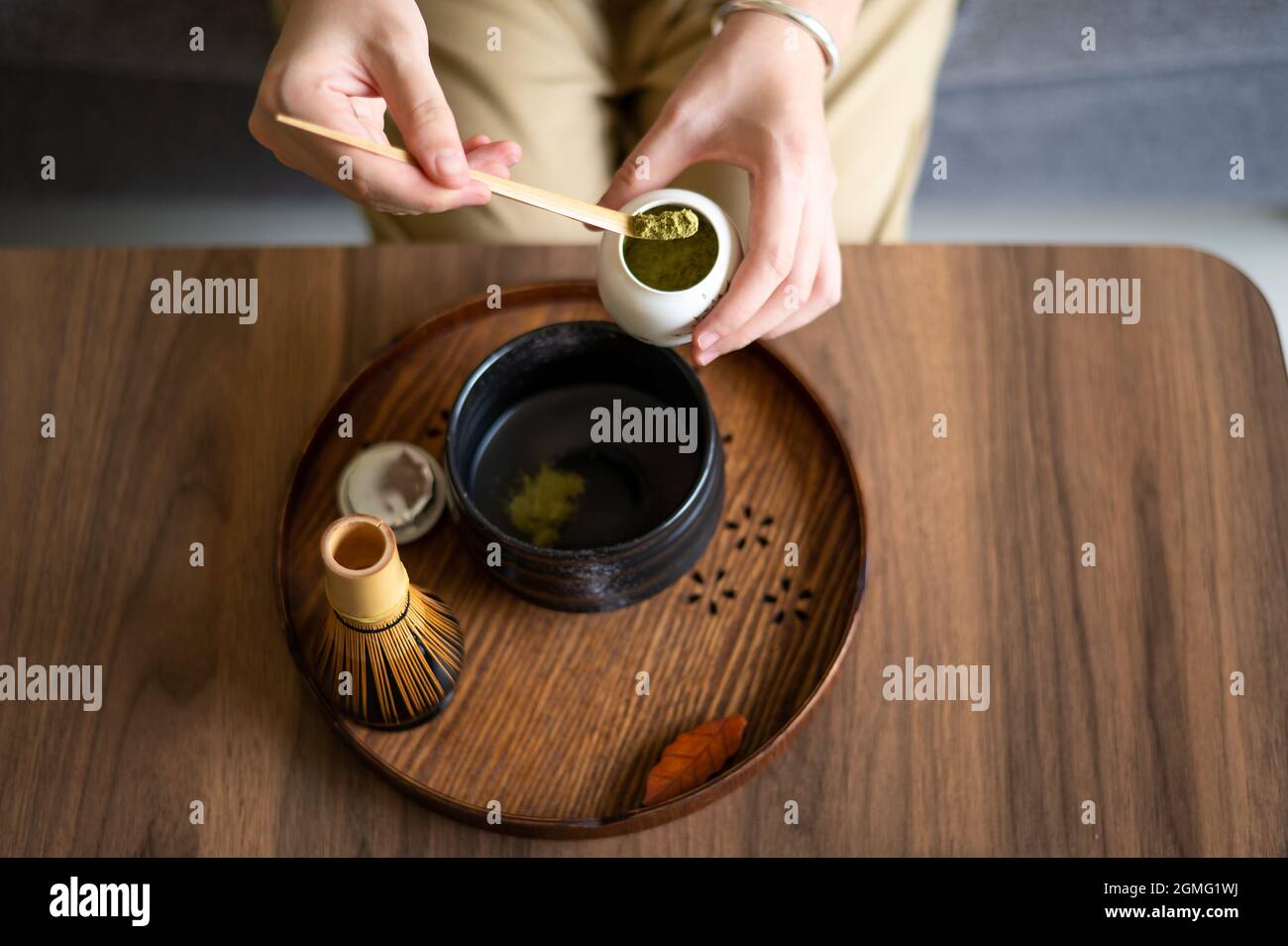 Frau, die zu Hause einen japanischen Matcha-Grüntee mit traditionellem Bambus-Set für Teezeremonien zubereitet, während sie zu Hause auf dem Sofa sitzt. Stockfoto