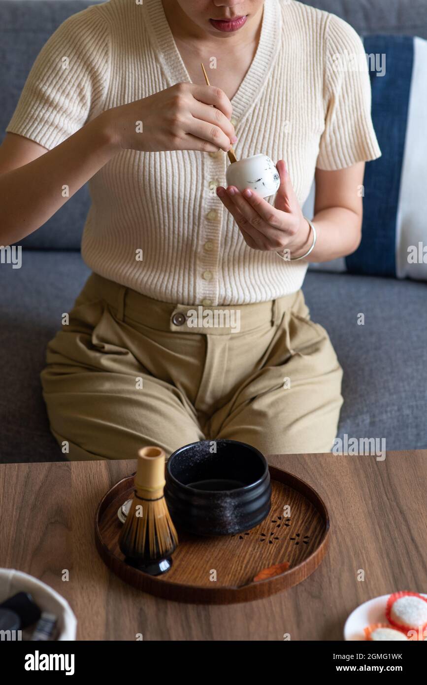Frau, die zu Hause einen japanischen Matcha-Grüntee mit traditionellem Bambus-Set für Teezeremonien zubereitet, während sie zu Hause auf dem Sofa sitzt. Stockfoto