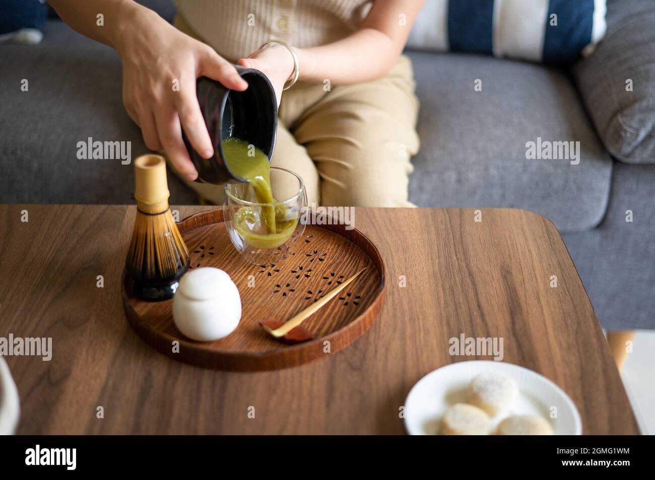 Frau gießt bereite japanische Matcha grünen Tee Getränk zu Hause mit traditionellen Tee Zeremonie Bambus-Set, während sie auf dem Sofa zu Hause sitzen. Stockfoto