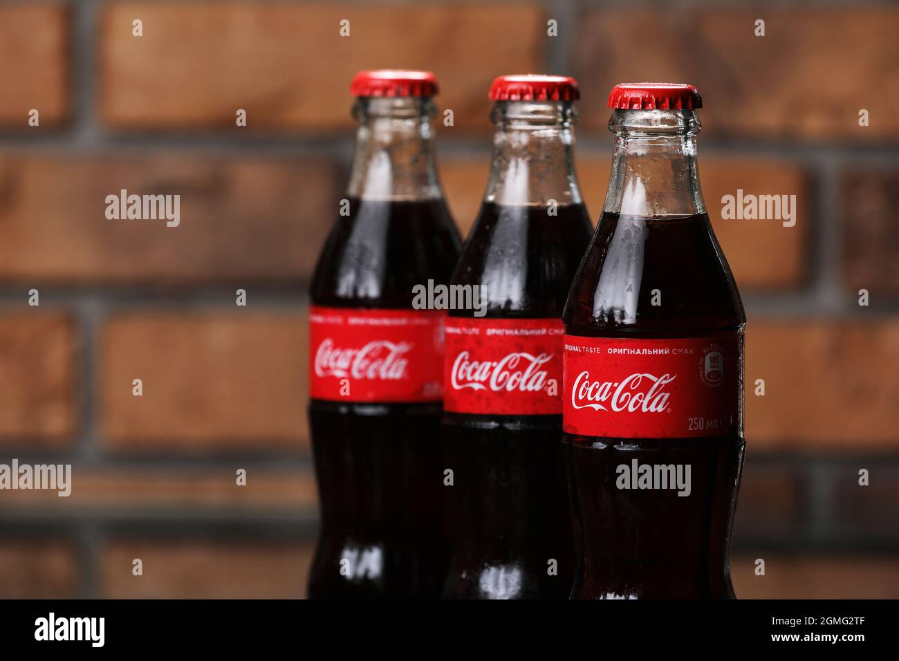 RIVNE, UKRAINE JUNI 26 2020: Drei klassische Glasflaschen von Coca-Cola auf Backsteinwand. Dosen von Coca-Cola. Stockfoto