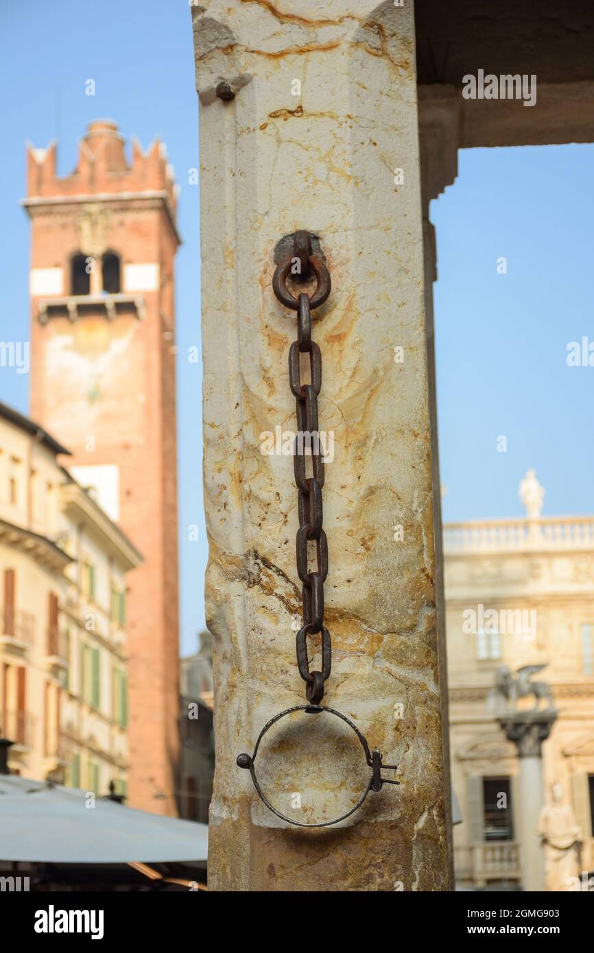 Mittelalterliche Steinsäule auf dem Stadtplatz, mit rostigen Fesseln für Sklaven und Kriminelle. Der Turm ist im Hintergrund. Stockfoto