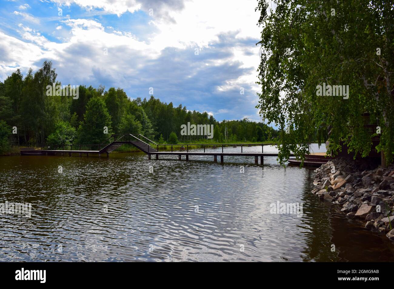 Eine große Holzbrücke über den Fluss mit einem Platz für Boote, unter dem man segeln kann. Die Ufer des Flusses sind mit Stein gesäumt. Vor dem Hintergrund eines b Stockfoto