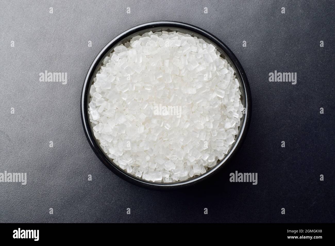 Kristallzucker in schwarzer Schale auf schwarzem Hintergrund Stockfoto