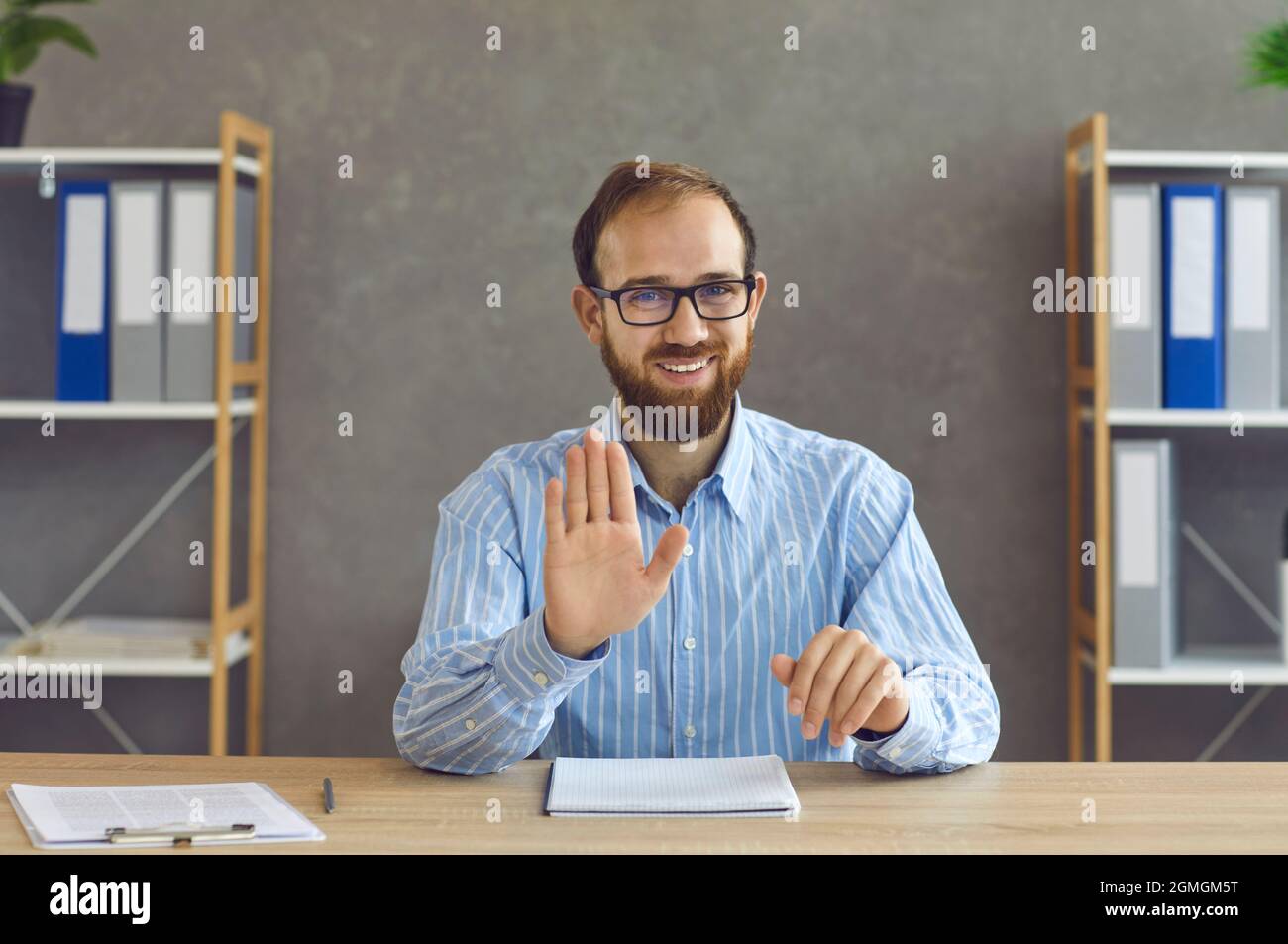 Der Millennial-Mann, der am Schreibtisch des Heimbüros sitzt und auf die Kamera schaut, zeigt eine Stop-Geste Stockfoto